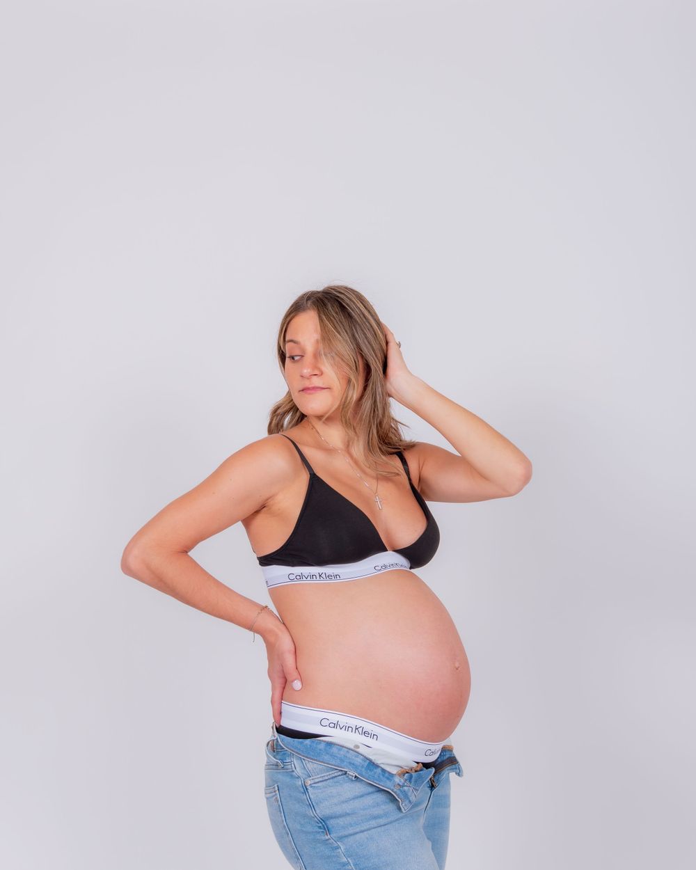 Side view of an expectant mother in black bra and jeans showing her pregnant belly.