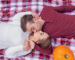 Couple sharing intimate moment on plaid blanket with pumpkin decoration.