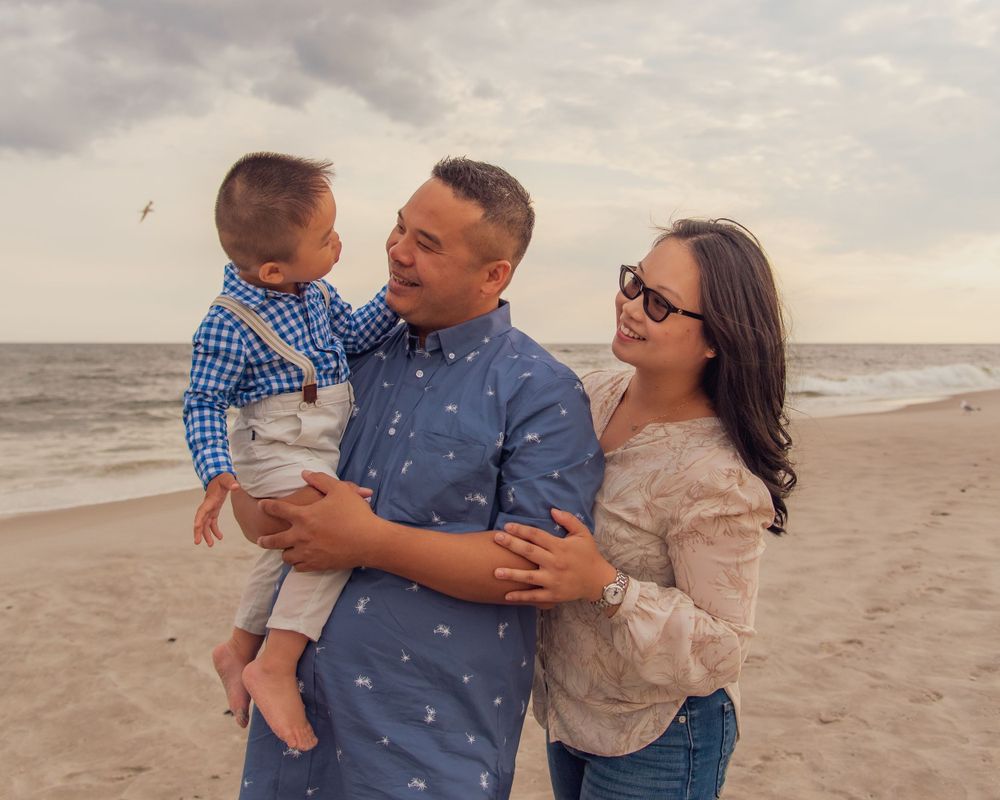 Happy family posing together on a beach at sunset with ocean waves in the background.