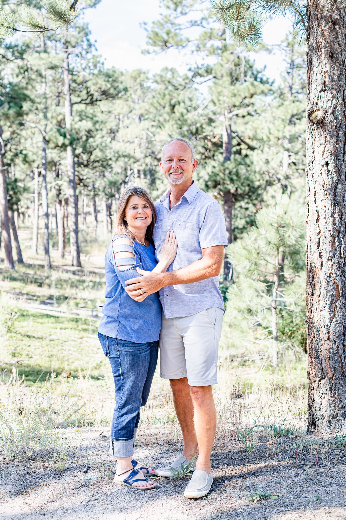 Husband and wife stand close together among the trees in Black Forest, Colorado.