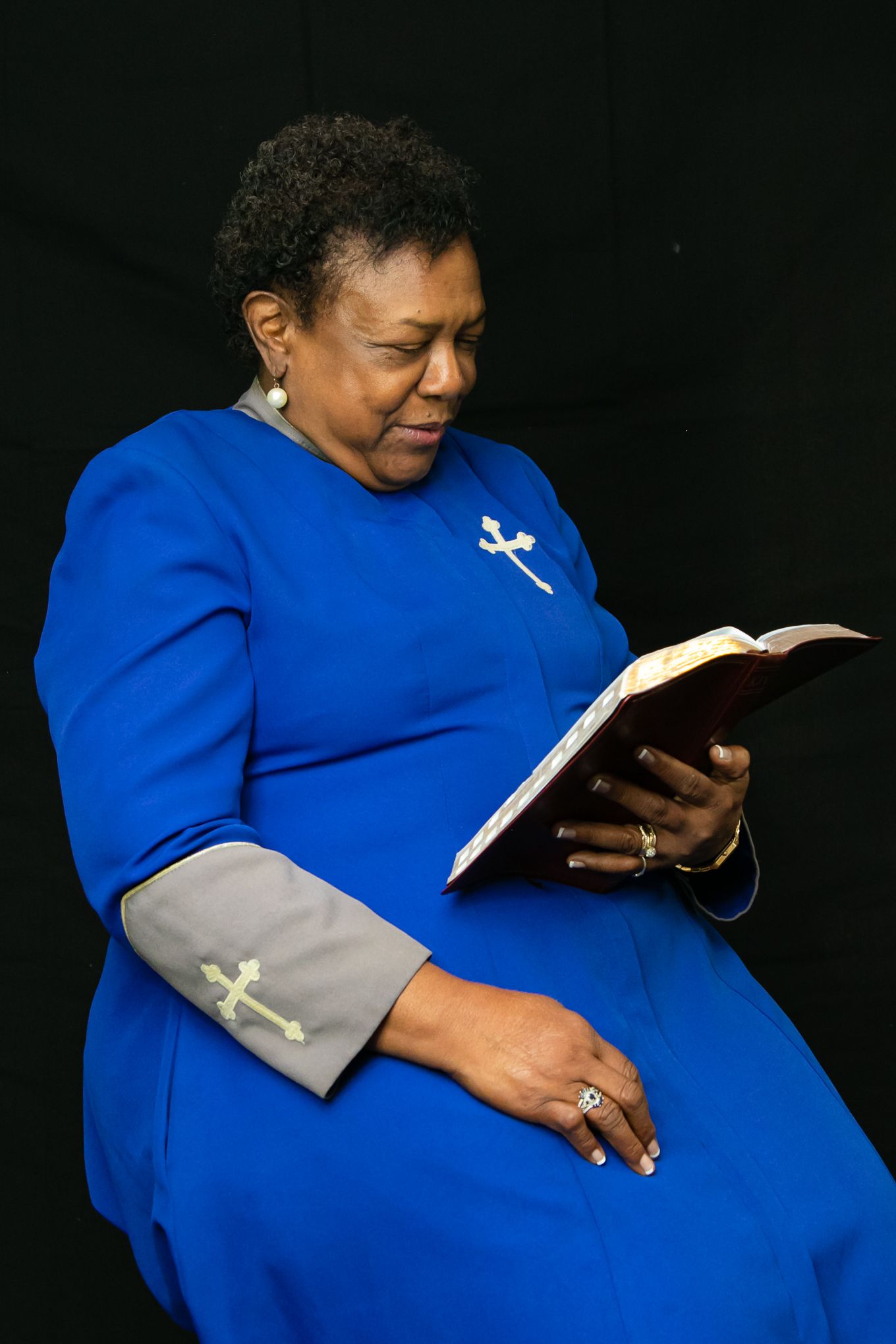 Woman wearing bright blue dress reads from book while seated.