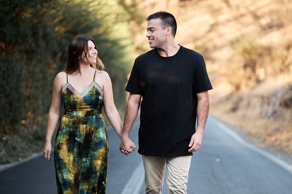 A couple holding hands while walking together on a scenic mountain road.