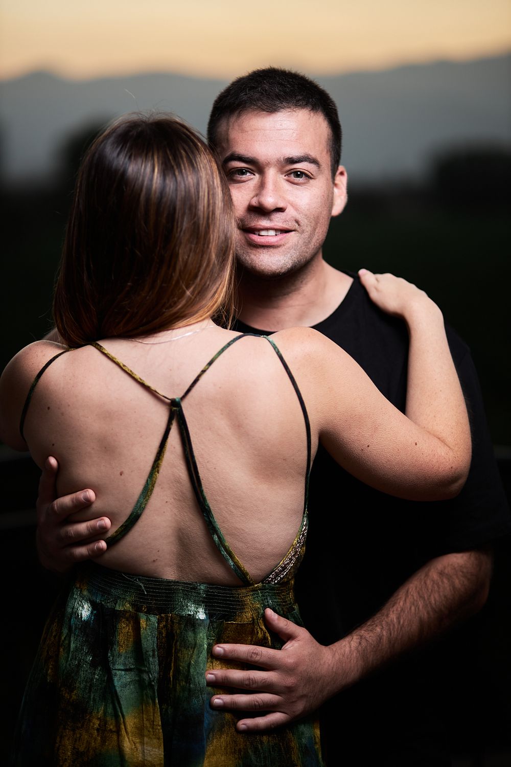 A romantic sunset portrait of a couple in an outdoor setting with mountains in background.