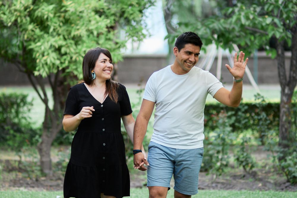 Playful couple laughing together in casual attire while walking through a green garden.