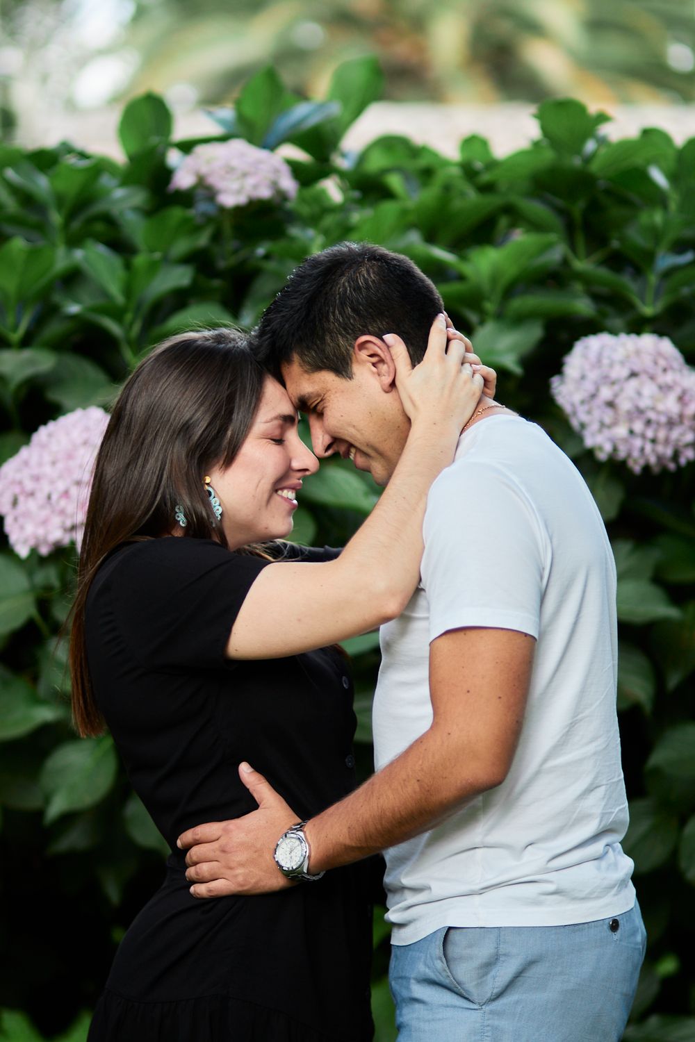 Intimate couple embracing among blooming pink hydrangea bushes in a garden setting.
