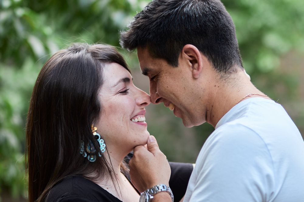 A romantic couple shares an intimate moment outdoors with natural greenery in the background.
