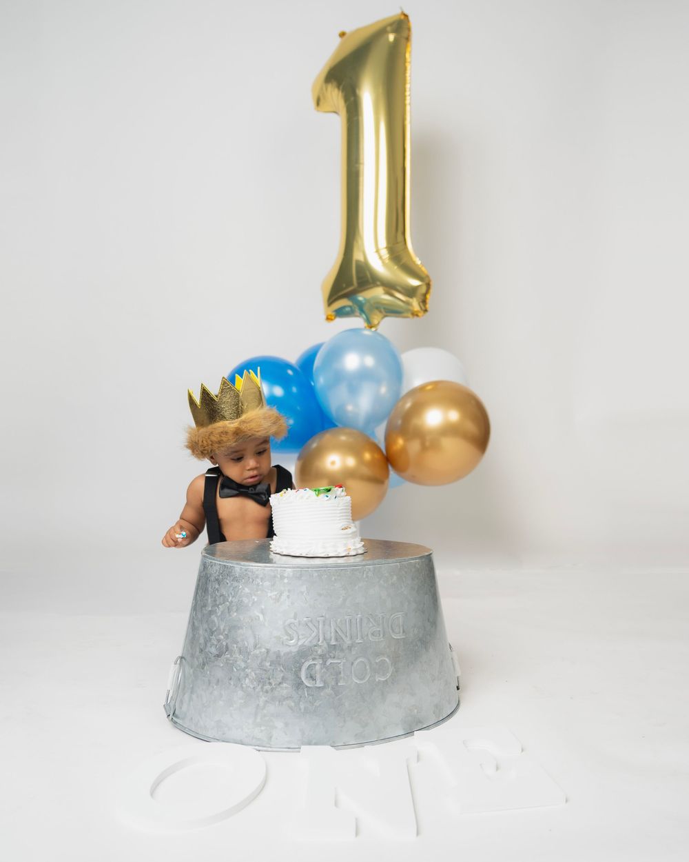 First birthday setup with gold number one balloon, crown, and blue and gold party decorations.