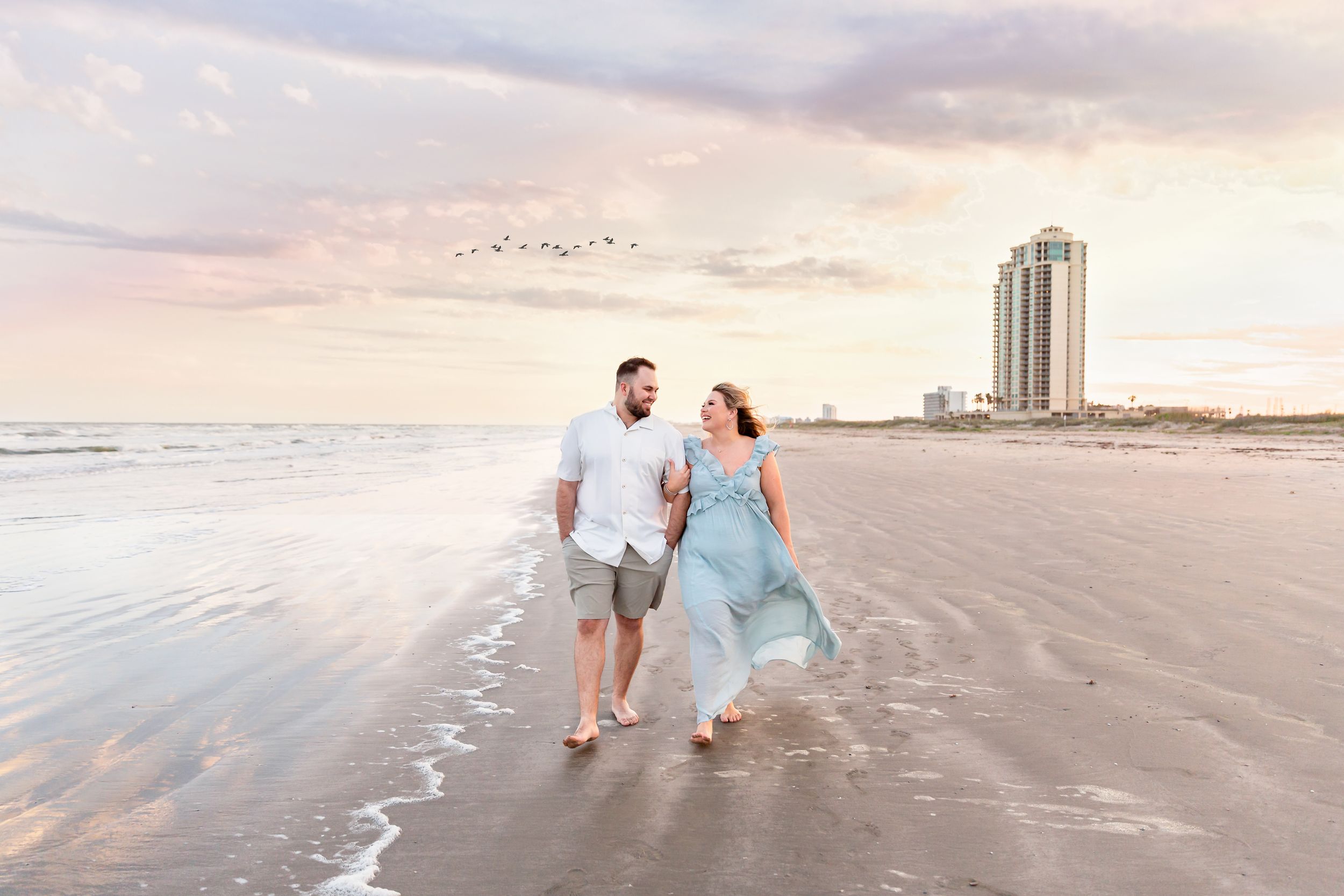 Couple walking arm in arm on the beach with a beautiful sunset in Galveston, TX.