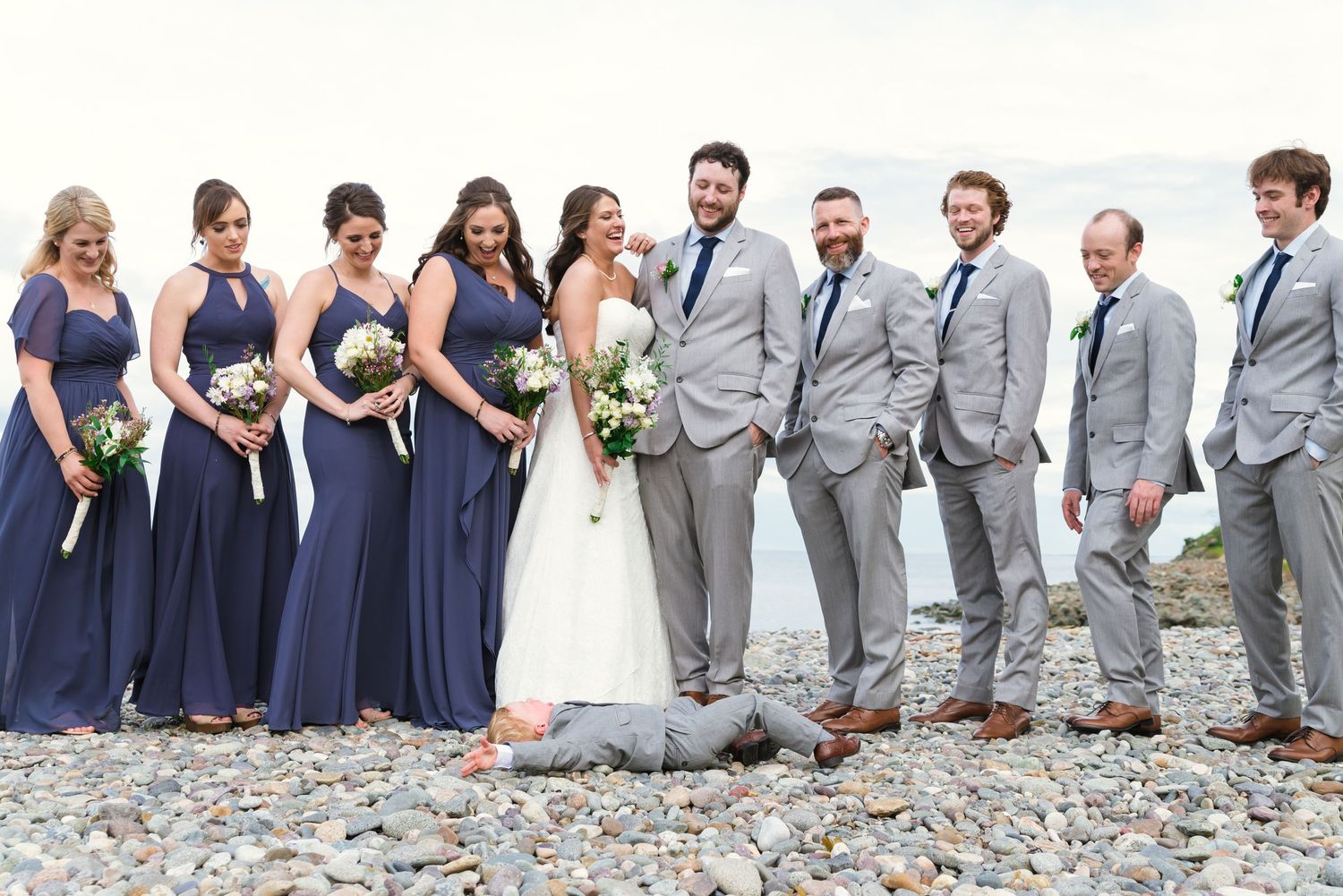 Large wedding party lined up wearing navy and gray attire for formal group photo.