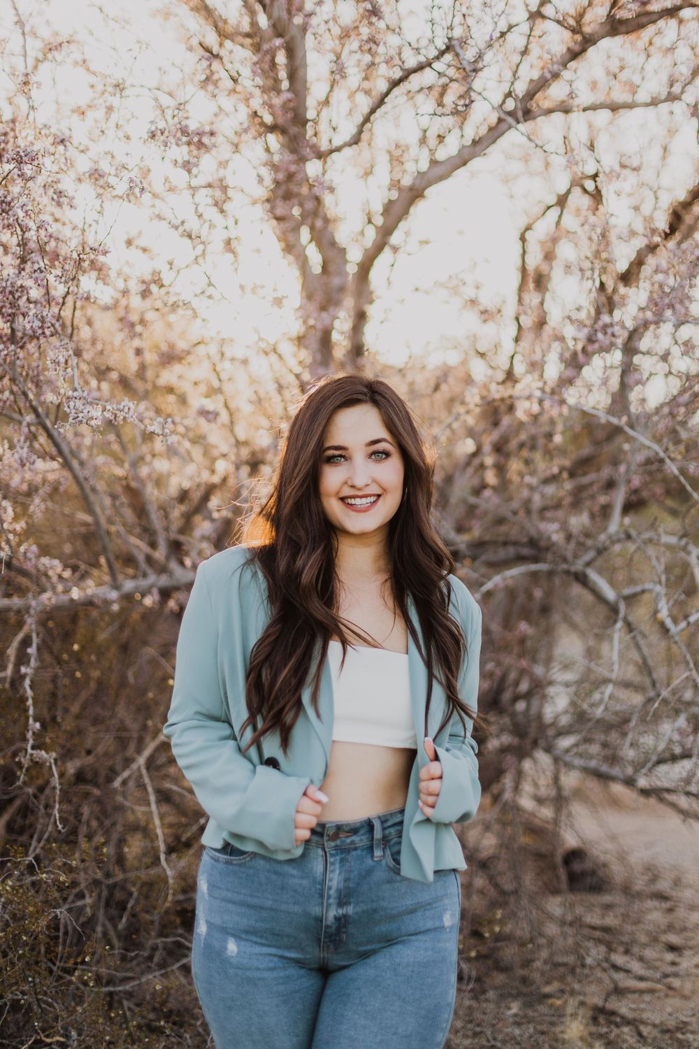 A person in a mint blazer and jeans poses outdoors against a backdrop of bare winter trees.