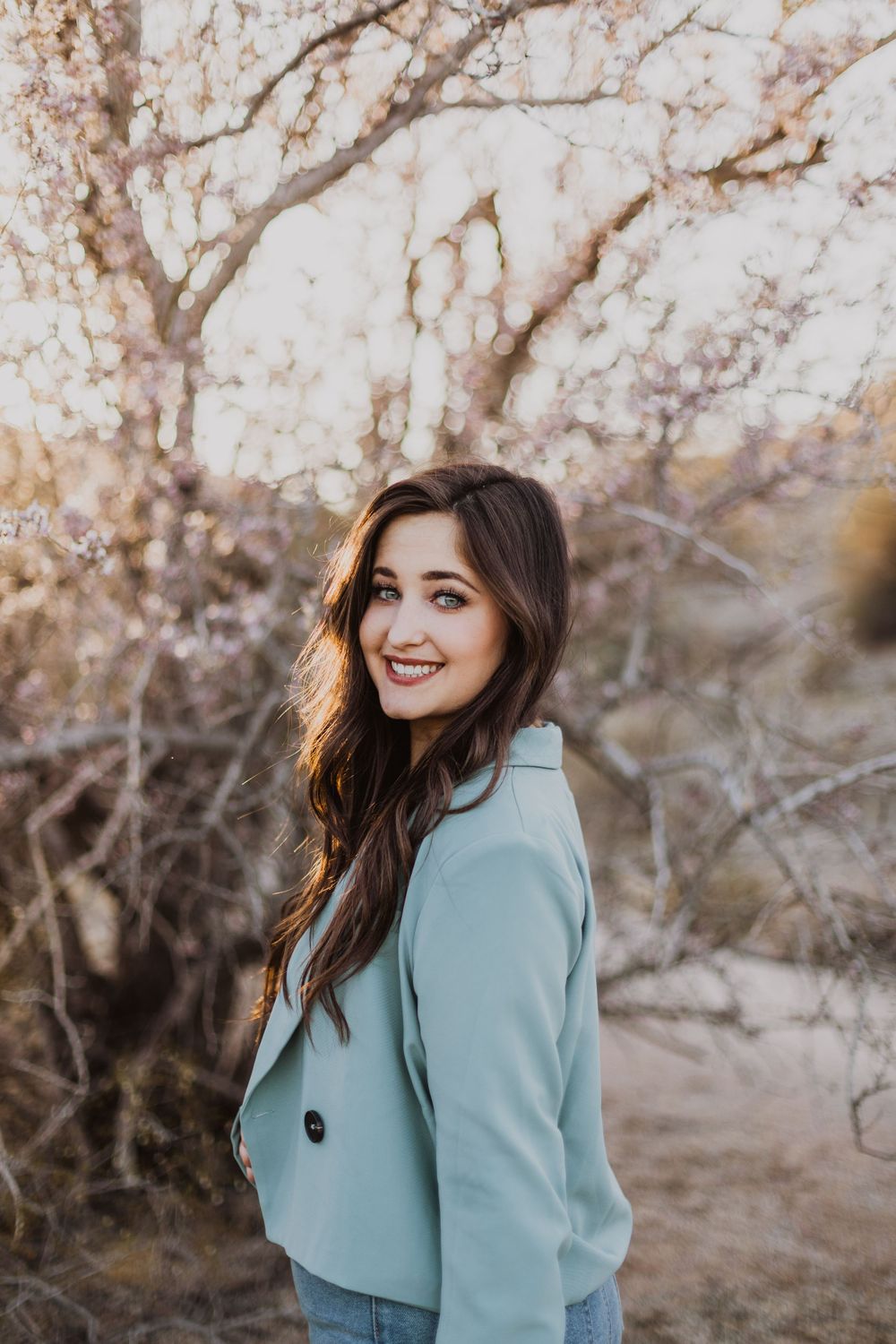 Outdoor photoshoot featuring someone in a mint blazer posing against blooming trees.