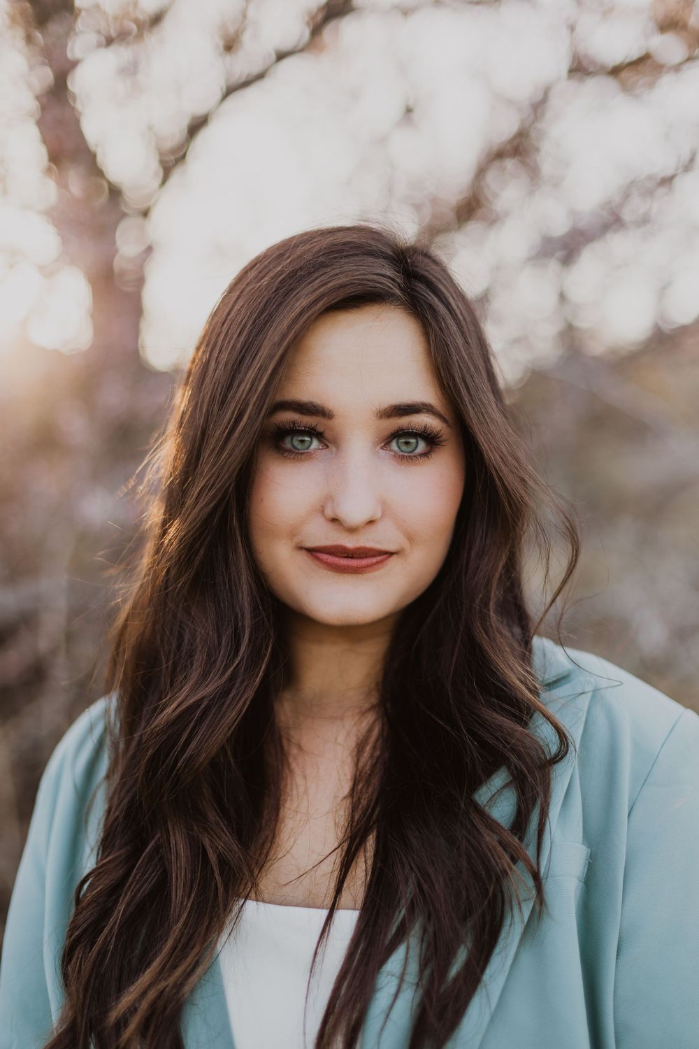 Close-up portrait shots with mint jacket and dark wavy hair against a blurred natural background.