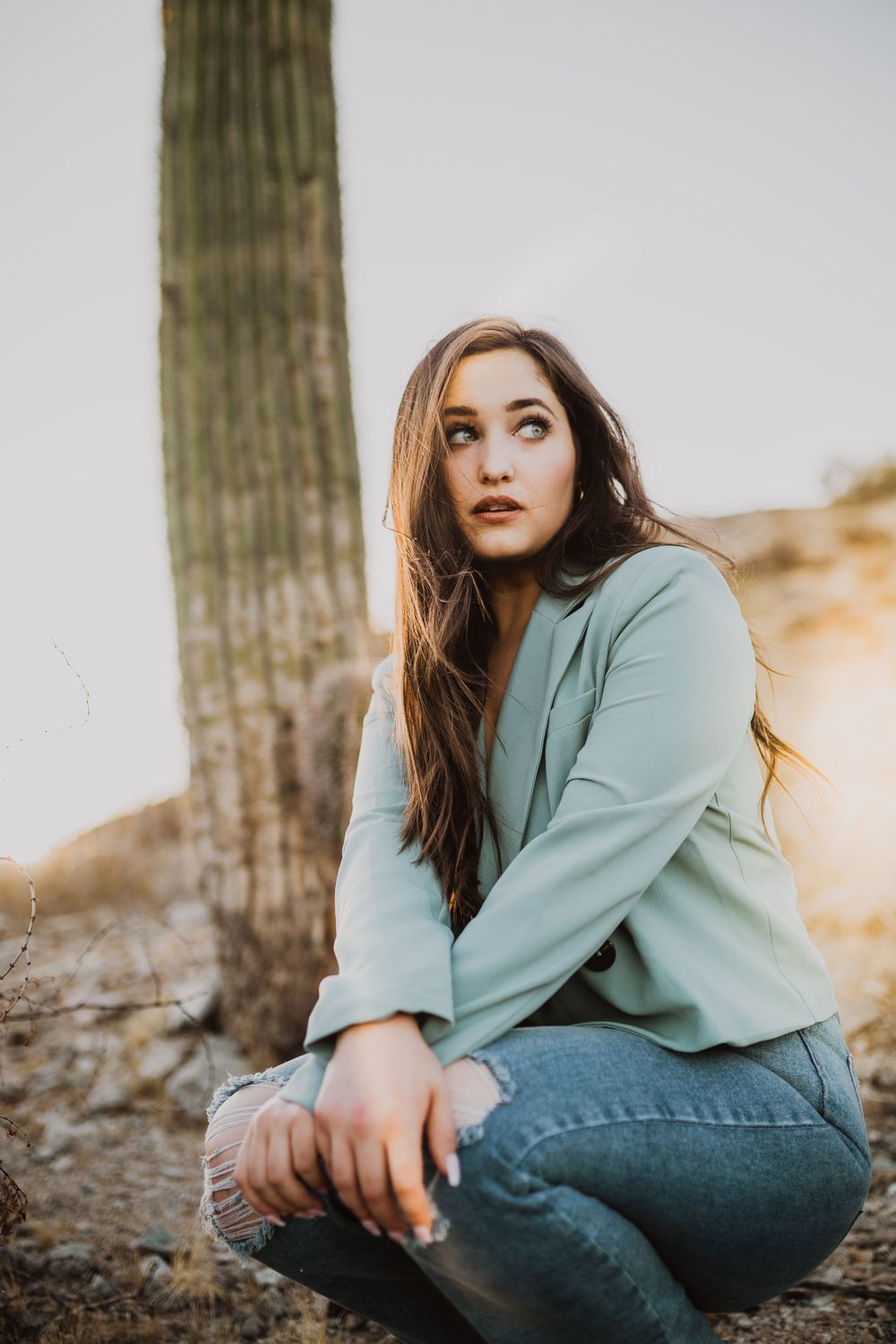 Casual poses by saguaro cactus wearing mint blazer and distressed jeans.