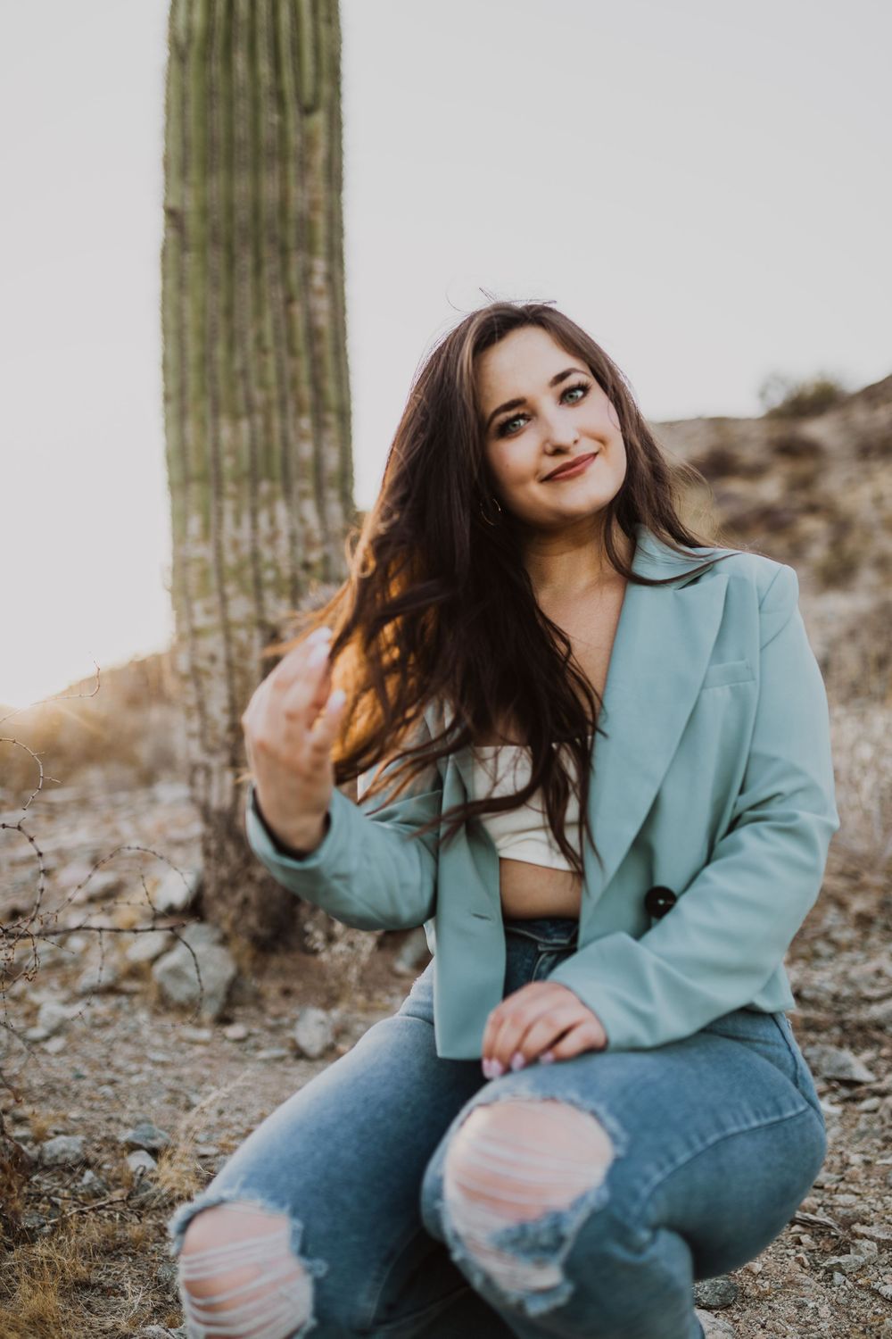 Relaxed outdoor portraits by desert cactus wearing ripped jeans and mint jacket.
