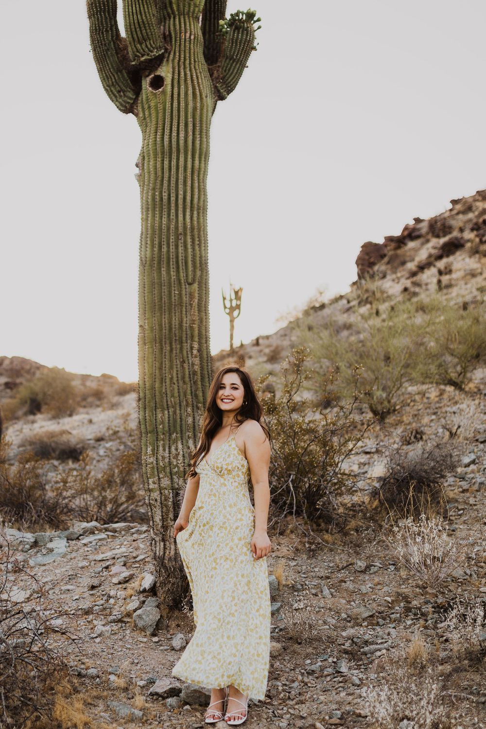 Desert photoshoot featuring floral sundress against rocky terrain and giant saguaro cactus.