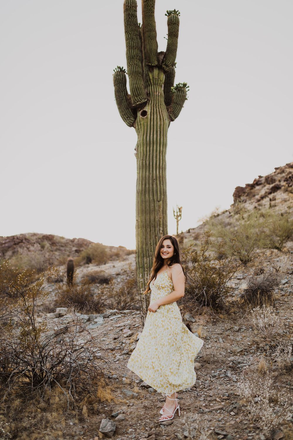 Desert fashion photography with flowing floral dress against rugged landscape and saguaro cactus.
