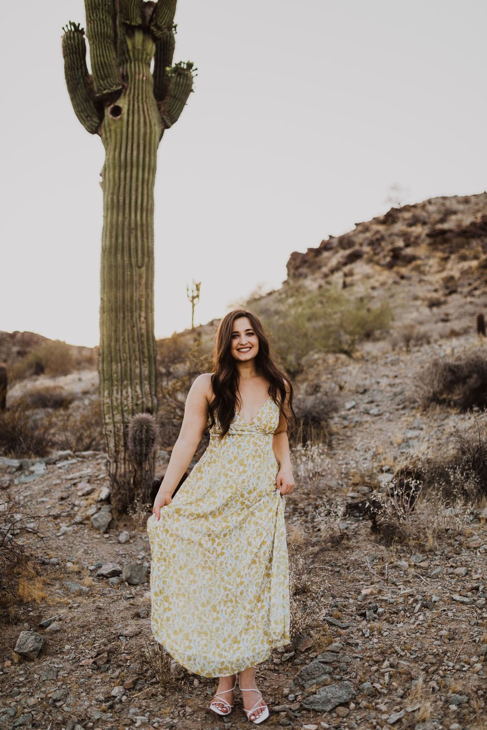 Playful desert photoshoot with floral dress and saguaro cactus in Arizona landscape.