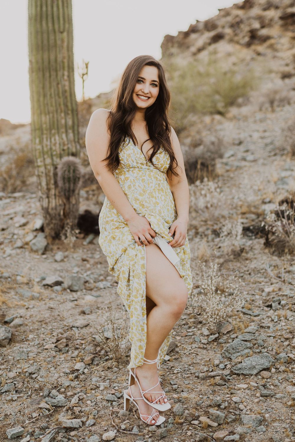 Candid desert photoshoot featuring floral dress and sandals against rocky terrain.