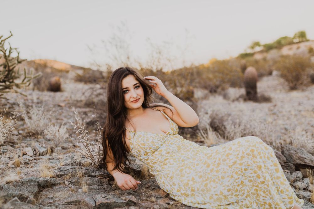 A floral maxi dress complements the natural desert landscape with mountains and cacti in the background.