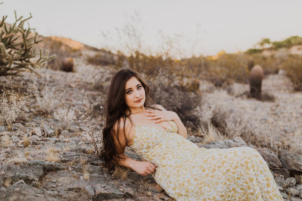 Elegant desert photoshoot featuring a yellow floral dress against rocky terrain and desert flora.
