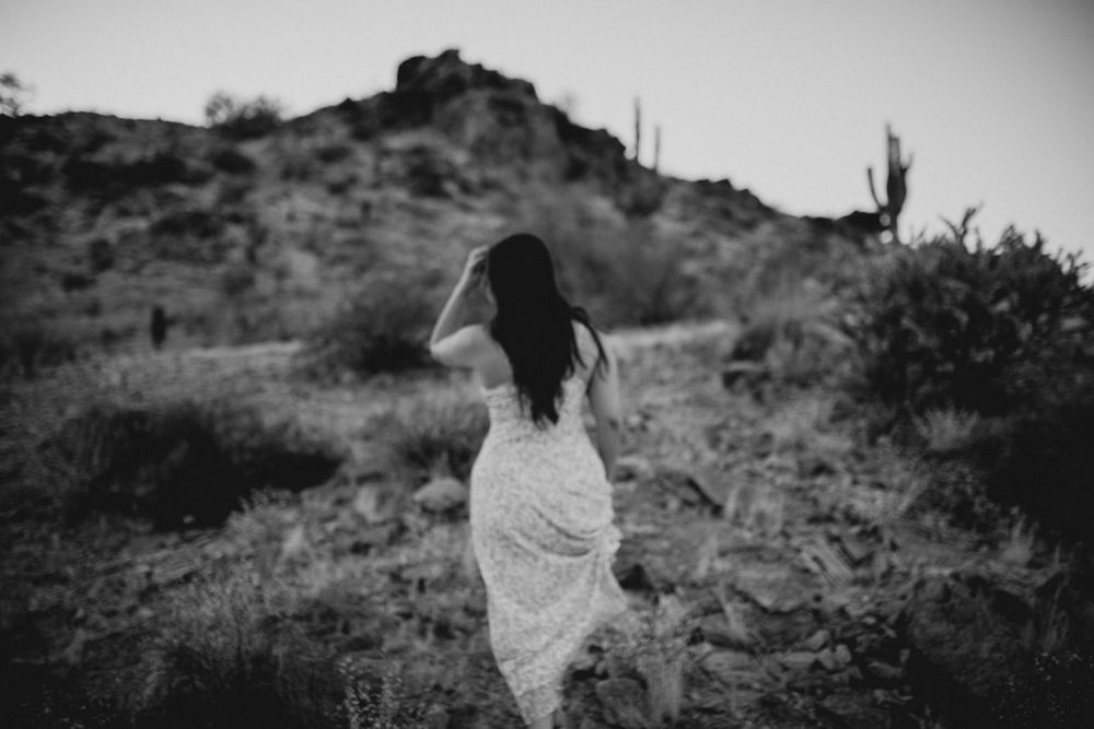 Black and white photo of a flowing dress contrasting against a desert hillside with saguaro silhouettes.