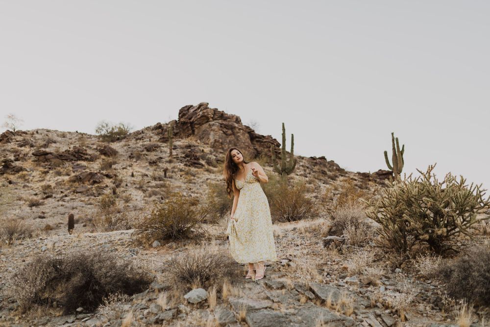 Light sundress creates ethereal movement against desert mountains and scattered cacti.
