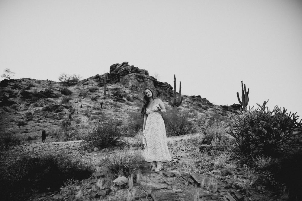Monochrome capture of a desert scene with dress flowing in the wind against rocky terrain.
