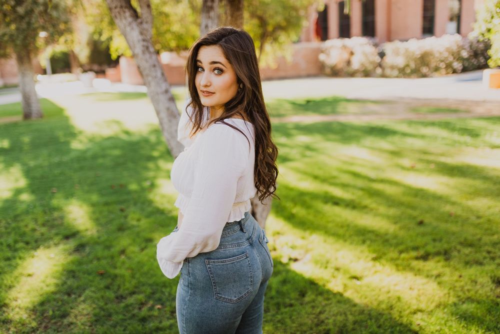A casual outdoor photoshoot featuring someone in a white blouse and denim against a natural backdrop.