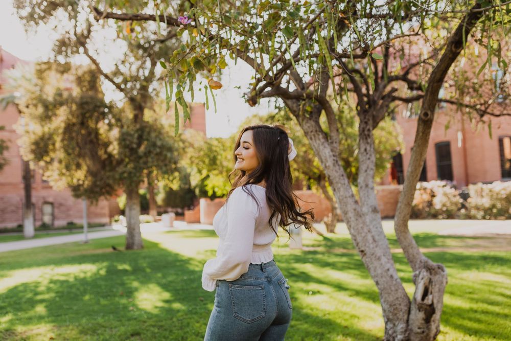 Natural light photography capturing someone in casual attire among trees on a grassy campus.
