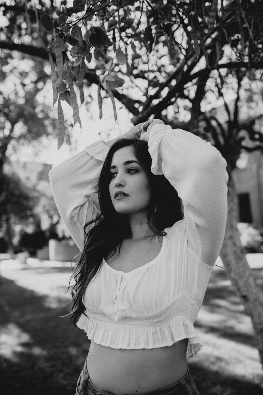 A dreamy black and white portrait series showing someone in a white ruffled top posing under tree branches.