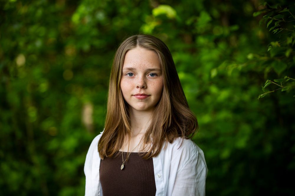 Portrait of young person in white cardigan against blurred green forest background.