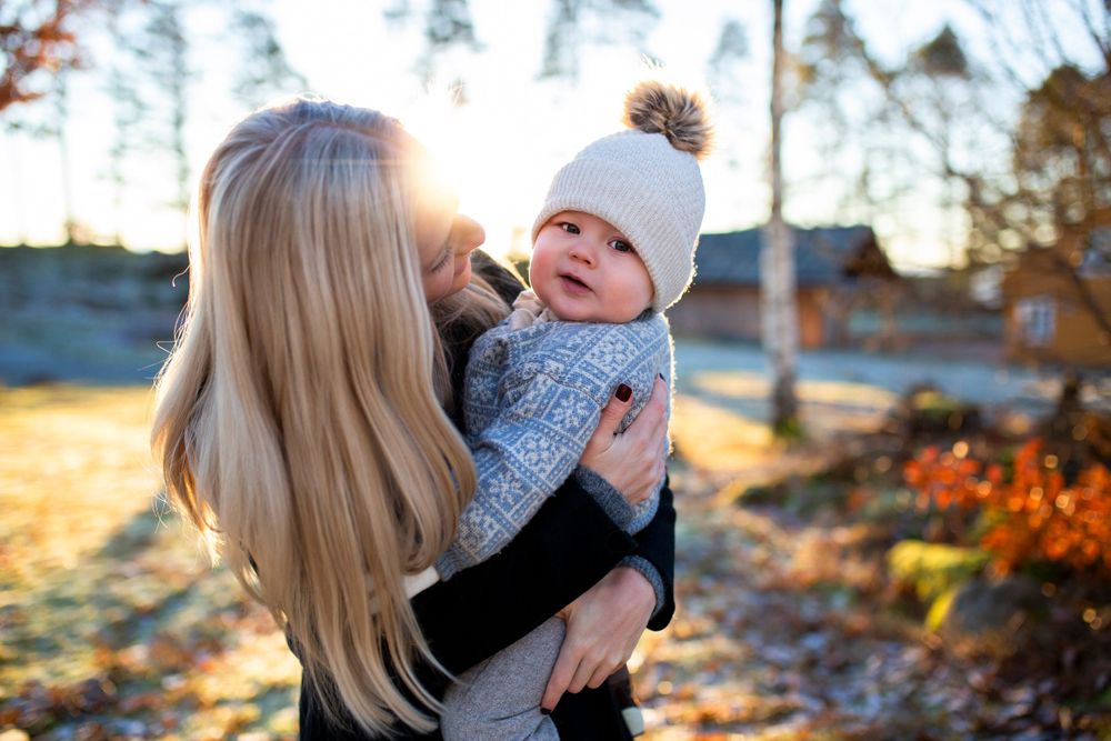 Parent and baby sharing joyful moment in golden sunset light with autumn foliage.