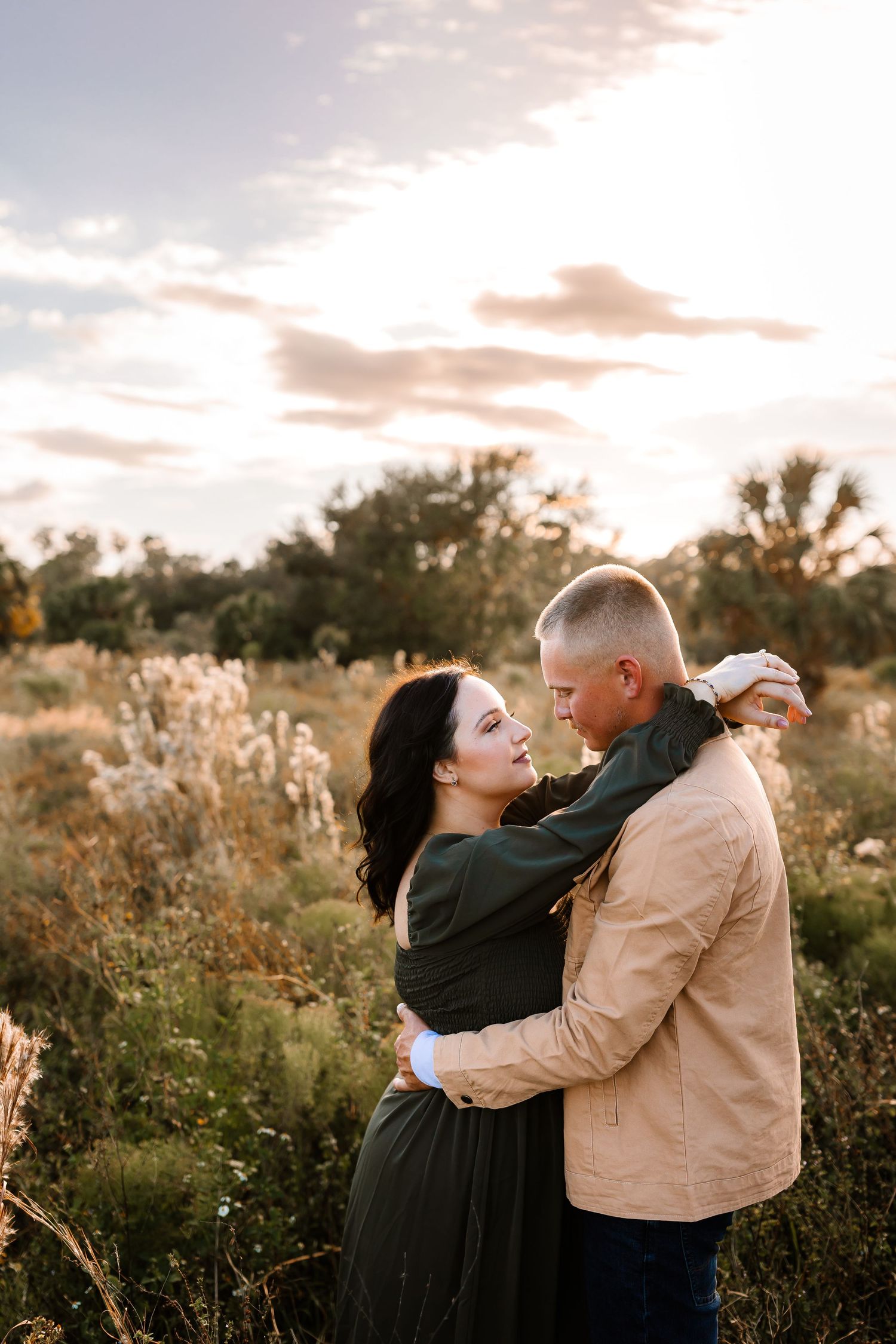 Romantic couple embracing in a wildflower field beneath a dramatic cloudy sky at sunset.
