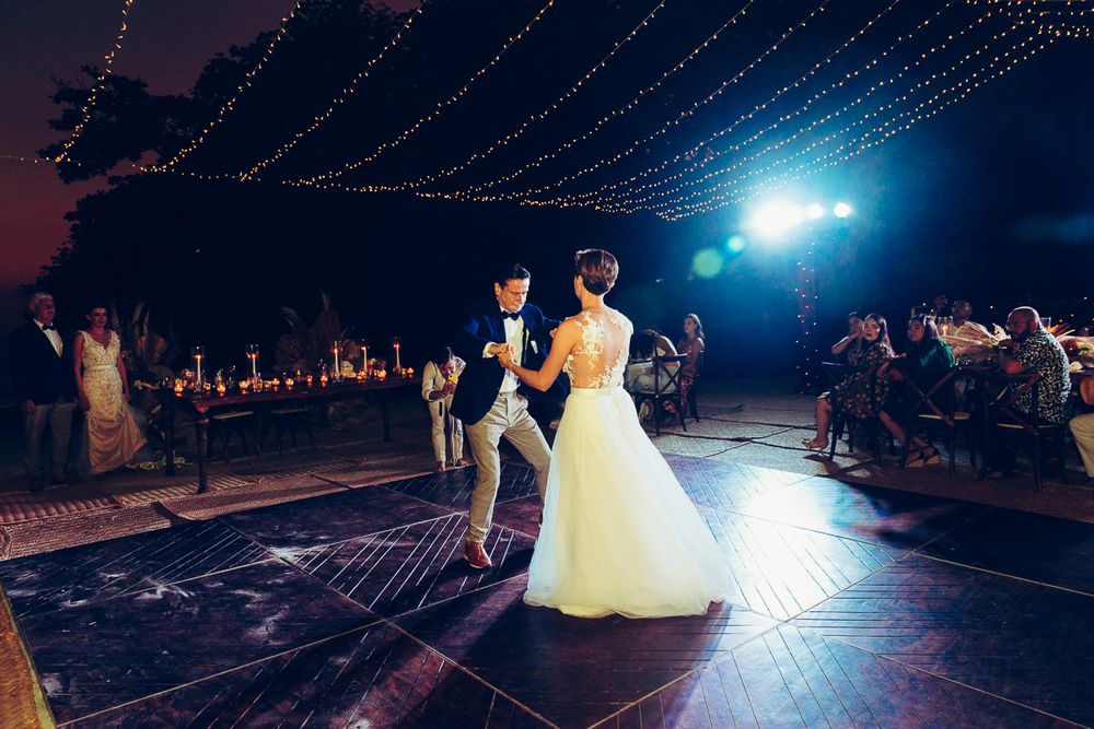Couple dancing on illuminated outdoor dance floor under string lights at night.