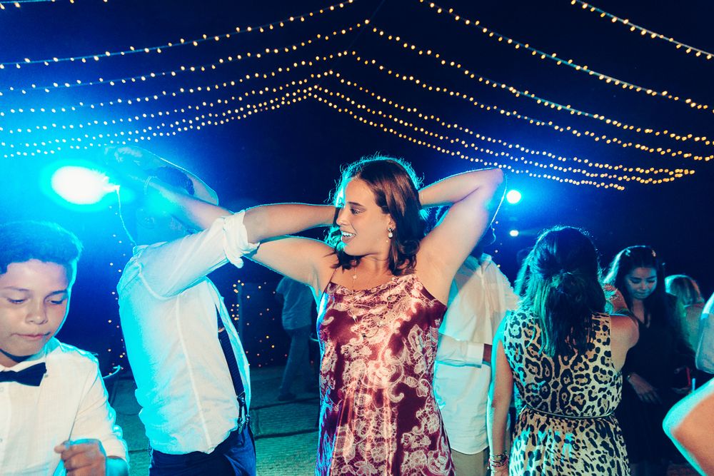 Lively dance floor scene with party guests dancing under blue lighting and string lights.