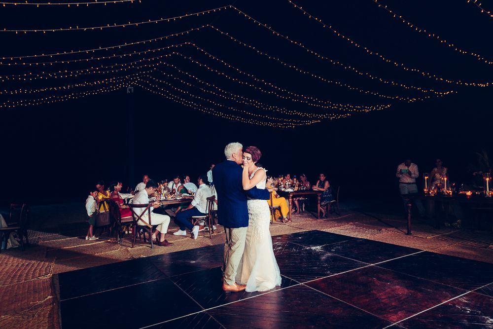 Wedding reception dance floor under canopy of string lights at night.