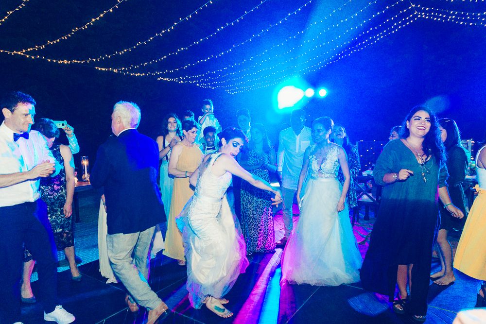 Wedding guests dancing and celebrating under dramatic blue lighting and hanging fairy lights.