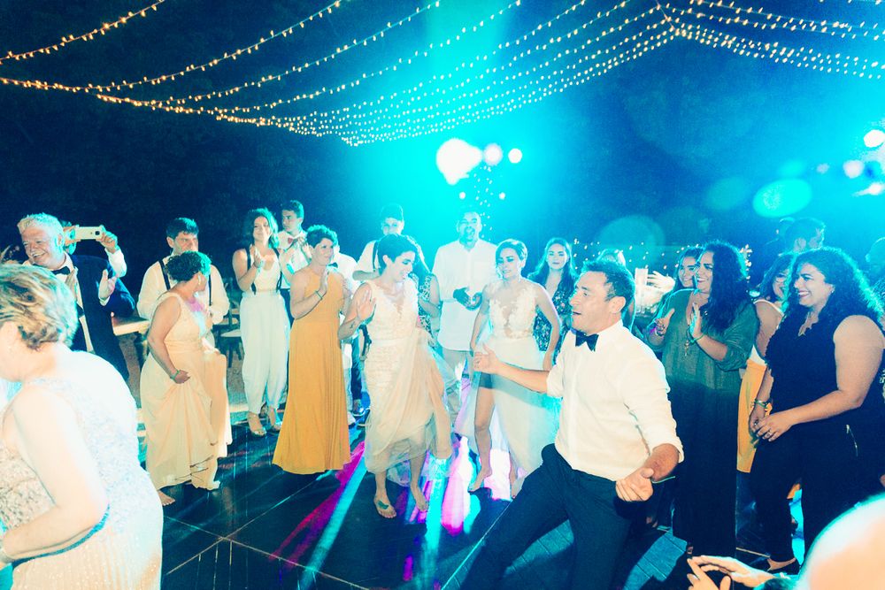 Energetic wedding reception with dancers under blue lights and string lighting creating a festive atmosphere.