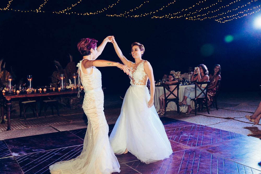 Two people in wedding attire dancing under string lights on outdoor dance floor.