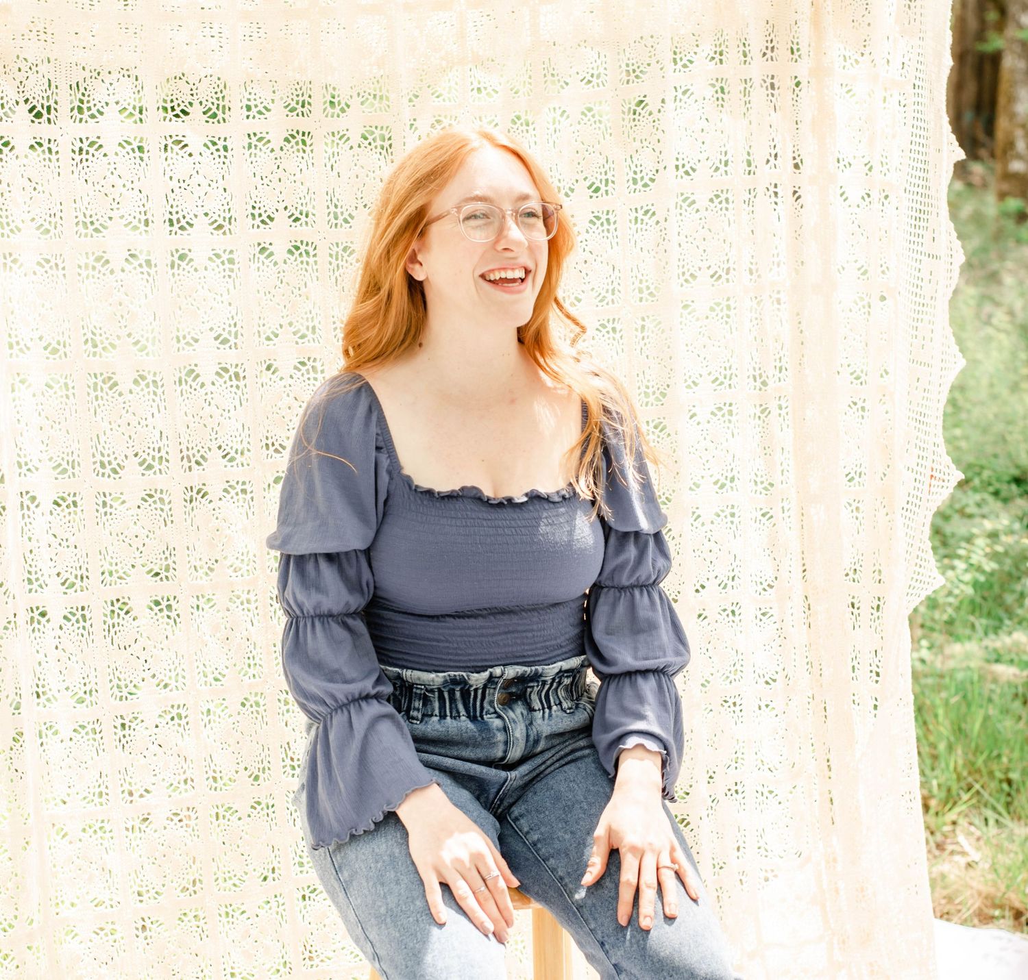 Portrait photo series with casual blue top and jeans seated on wooden stool against light backdrop.