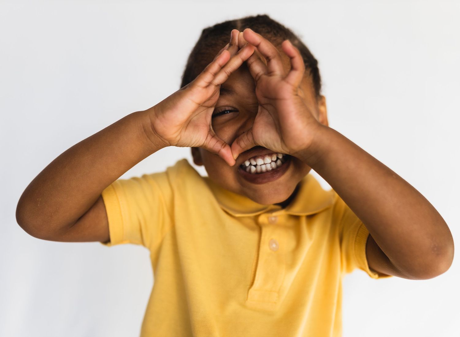Child in yellow polo shirt making playful gestures with hands near face.