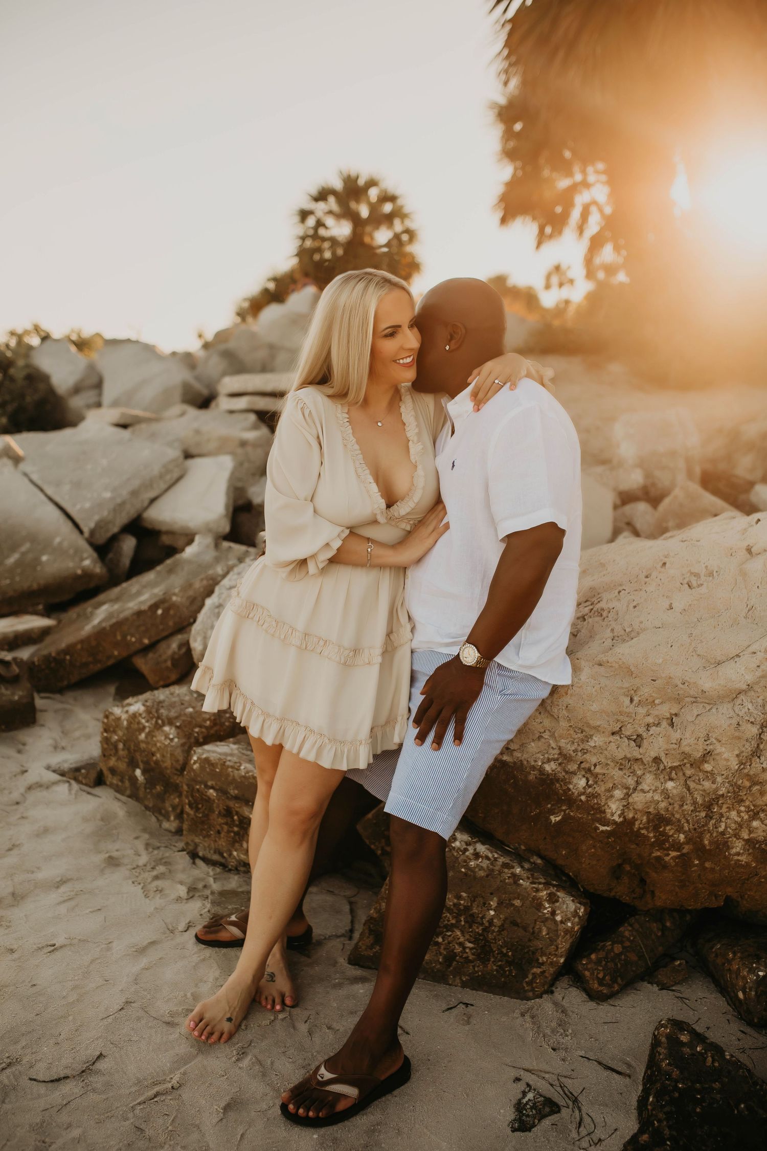 Affectionate couple embrace on beach rocks during warm sunset photoshoot.