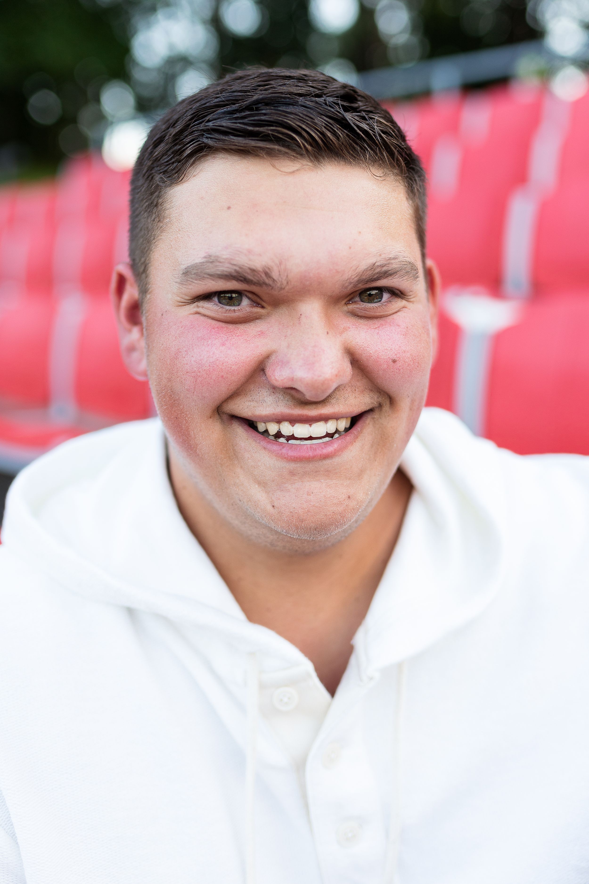 Portrait in white polo shirt against red stadium seats background.