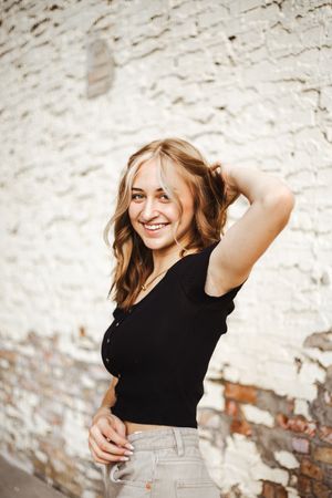 Casual portrait against white brick wall wearing black top and grey pants.