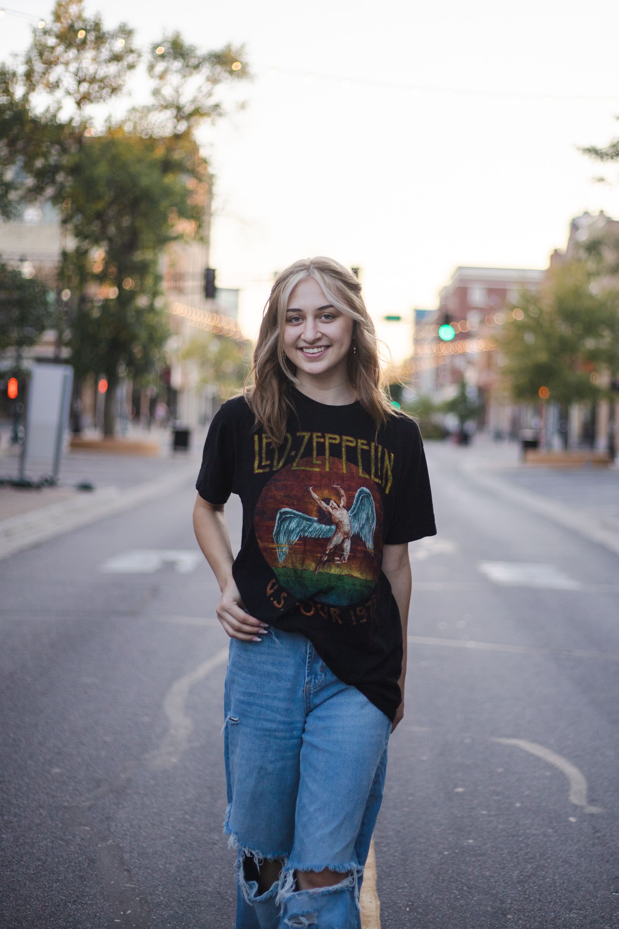 Woman wearing Led Zeppelin t-shirt and ripped jeans poses on an empty city street at dusk.
