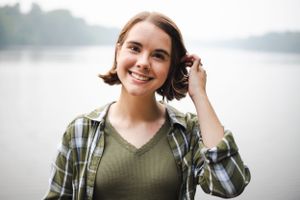 Casual outdoor portrait by a lake wearing a plaid flannel shirt and olive green top.