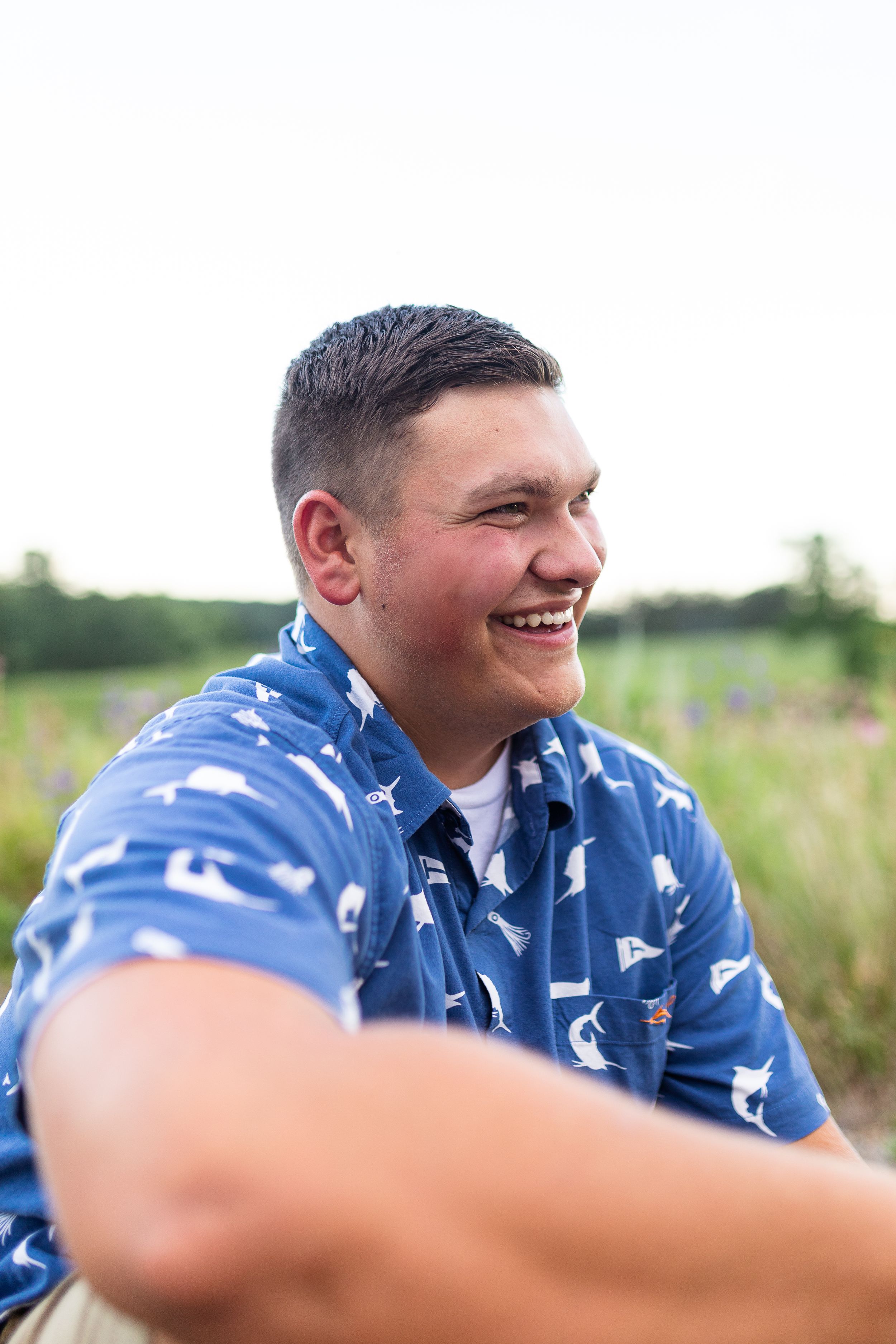 Person in blue patterned shirt laughs joyfully outdoors.