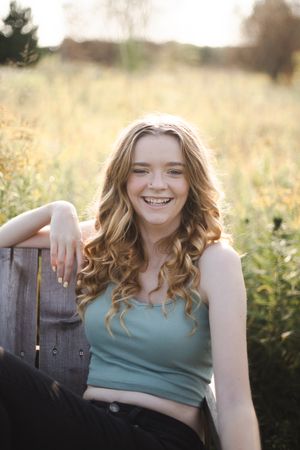 Woman in teal tank top sitting outdoors in a sunlit field with wildflowers.