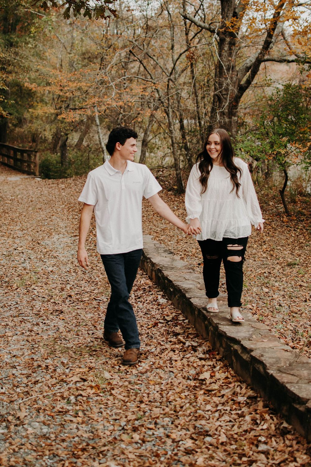 Couple in matching white tops walking together through fall woodland scenery.