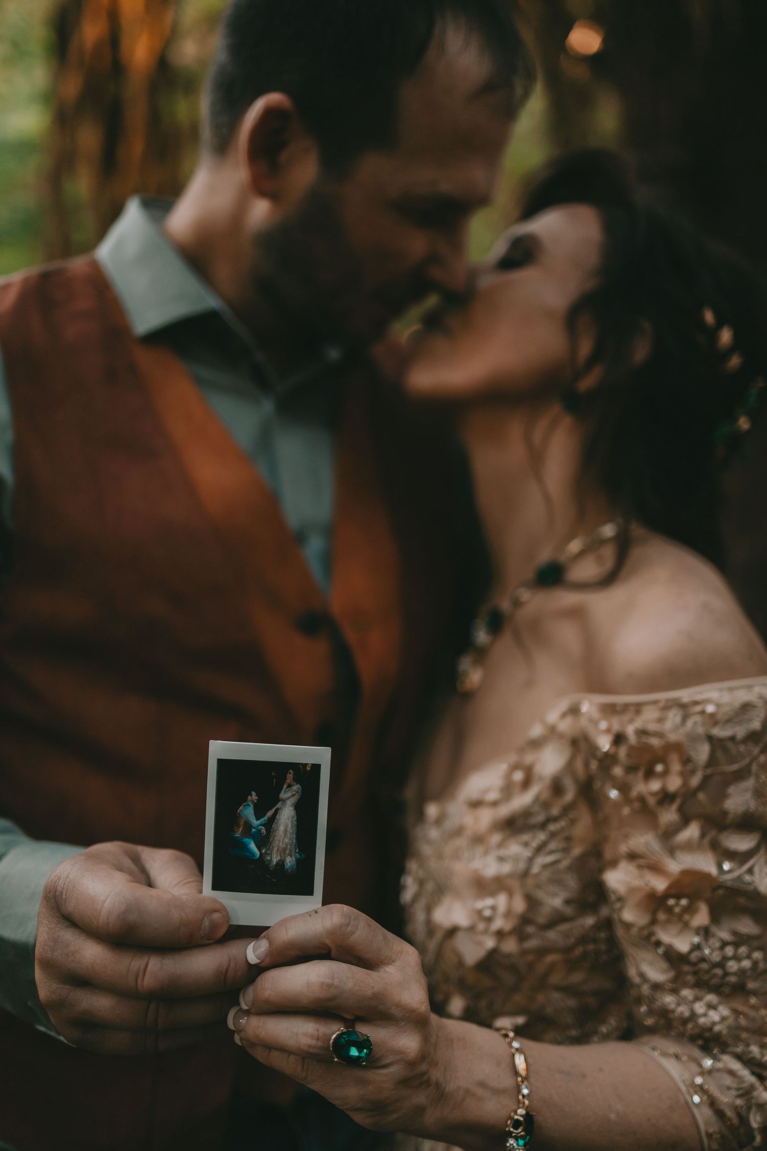 A man and woman in wedding attire kissing while both holding up a Polaroid picture of them The Hoh Rainforest Olympic National Park